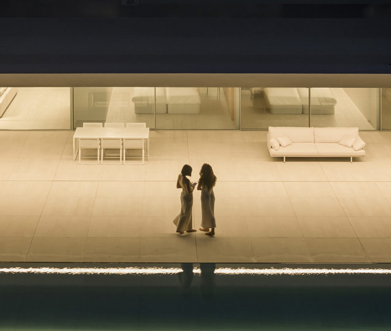 Minimalistyczny dom otoczony wzg&oacute;rzami i lasami. Na dachu – ogromna tafla wody.